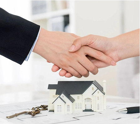 Two people shaking hands over a table with a house and keys.