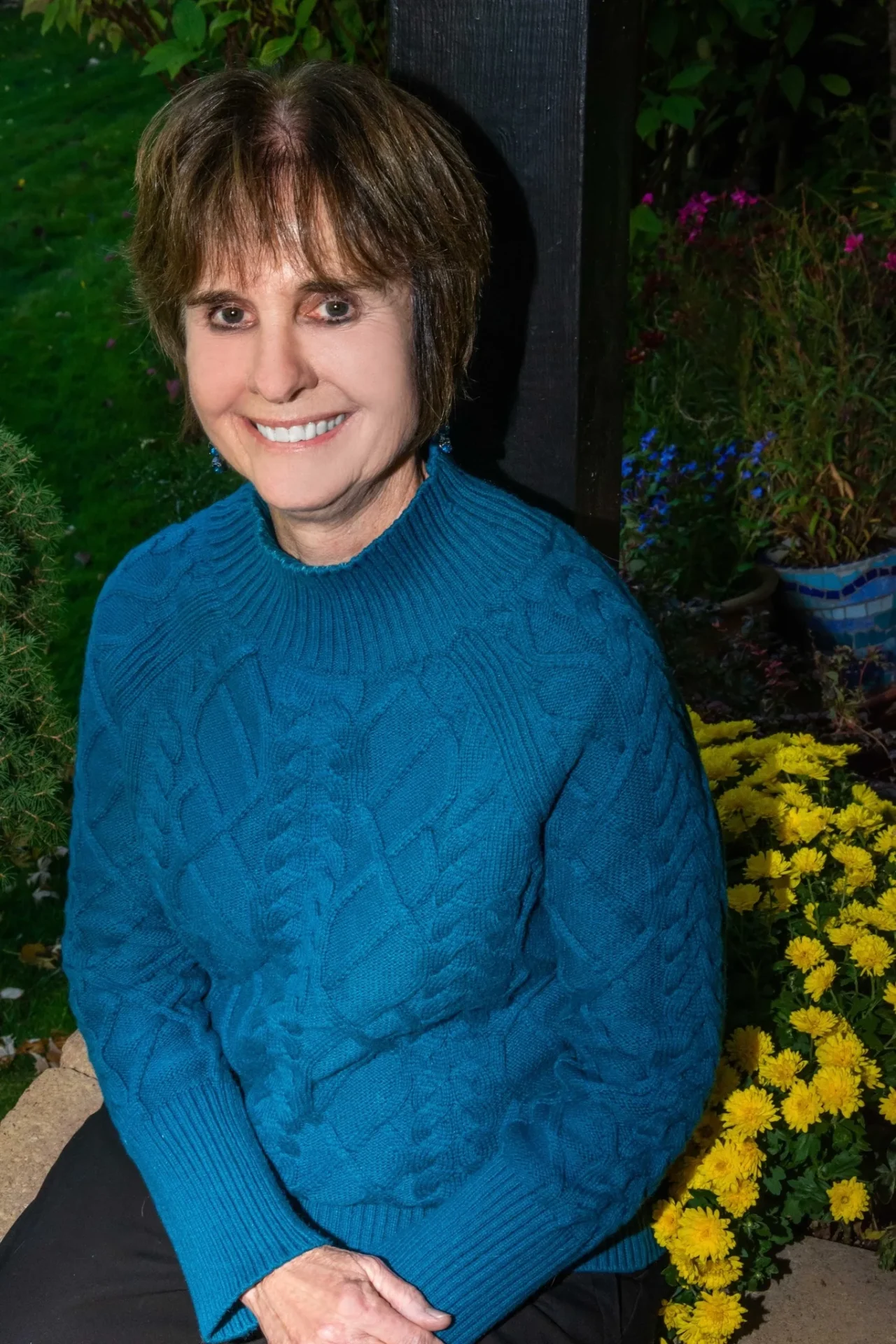 A woman in blue sweater standing next to yellow flowers.